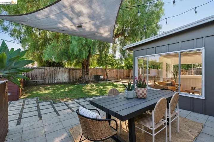 Expansive backyard featuring a paver patio with a shade sail, string lighting, a manicured lawn, and a wooden privacy fence