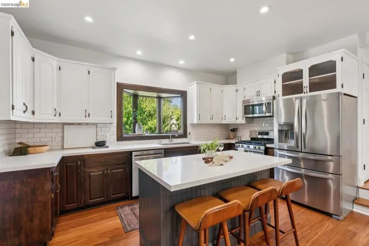 Contemporary kitchen featuring a central island, white upper cabinetry, rich wood-finish lower cabinetry, a white subway tile backsplash, and stainless steel appliances