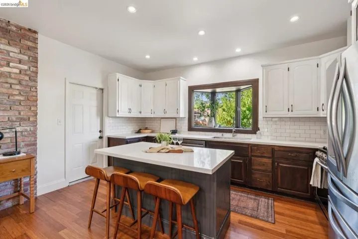 Kitchen featuring wood-finish flooring, a central island with countertop seating, white upper cabinetry, dark wood lower cabinetry, and a subway tile backsplash