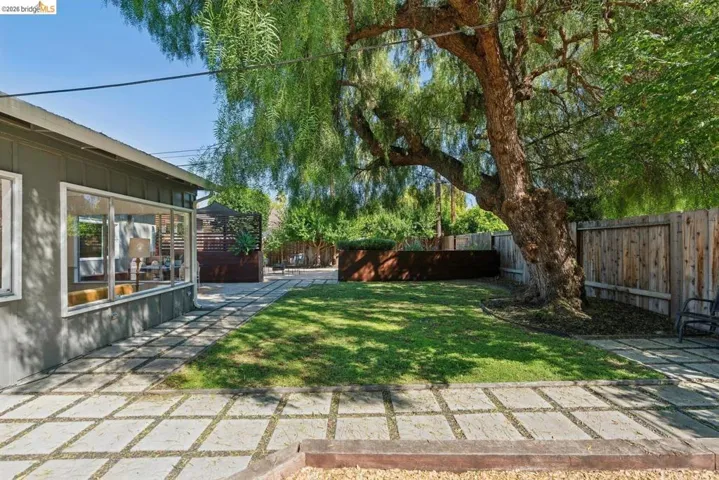 Landscaped backyard featuring a mature tree, a manicured lawn, and a stone paver patio