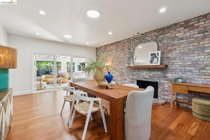 Exposed brick fireplace with a wood mantle, recessed lighting, wood-finish flooring, and sliding glass doors