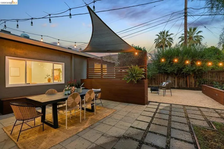 Outdoor patio area featuring a concrete paver and gravel surface, wood-tone privacy screening, and string lighting