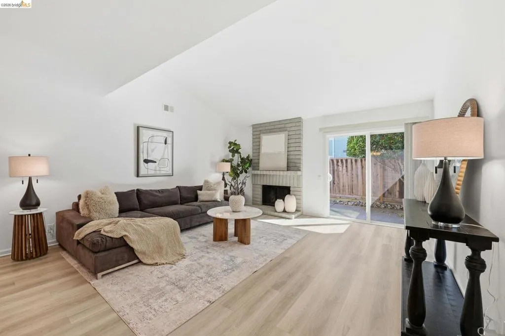 Vaulted ceiling living room featuring light wood-finish flooring, a brick fireplace, and sliding glass doors to the outdoor space