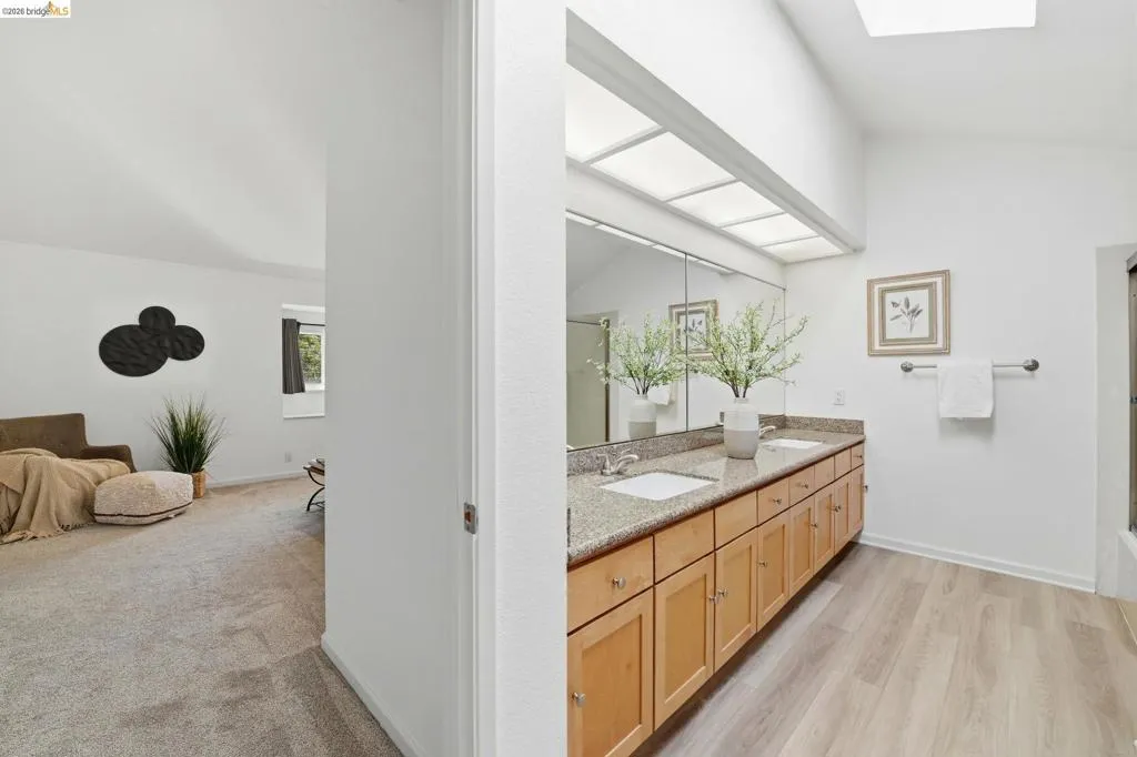 Bathroom featuring a double vanity with stone-finish countertop, light wood cabinetry, and dual undermount sinks