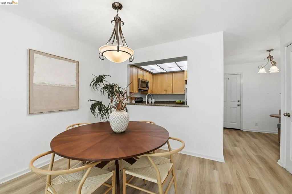 Dining area featuring wood-finish flooring, a contemporary chandelier, and a pass-through window to the kitchen