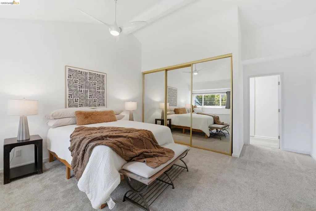 Bedroom featuring plush carpeting, a vaulted ceiling with a modern ceiling fan, and mirrored closet doors