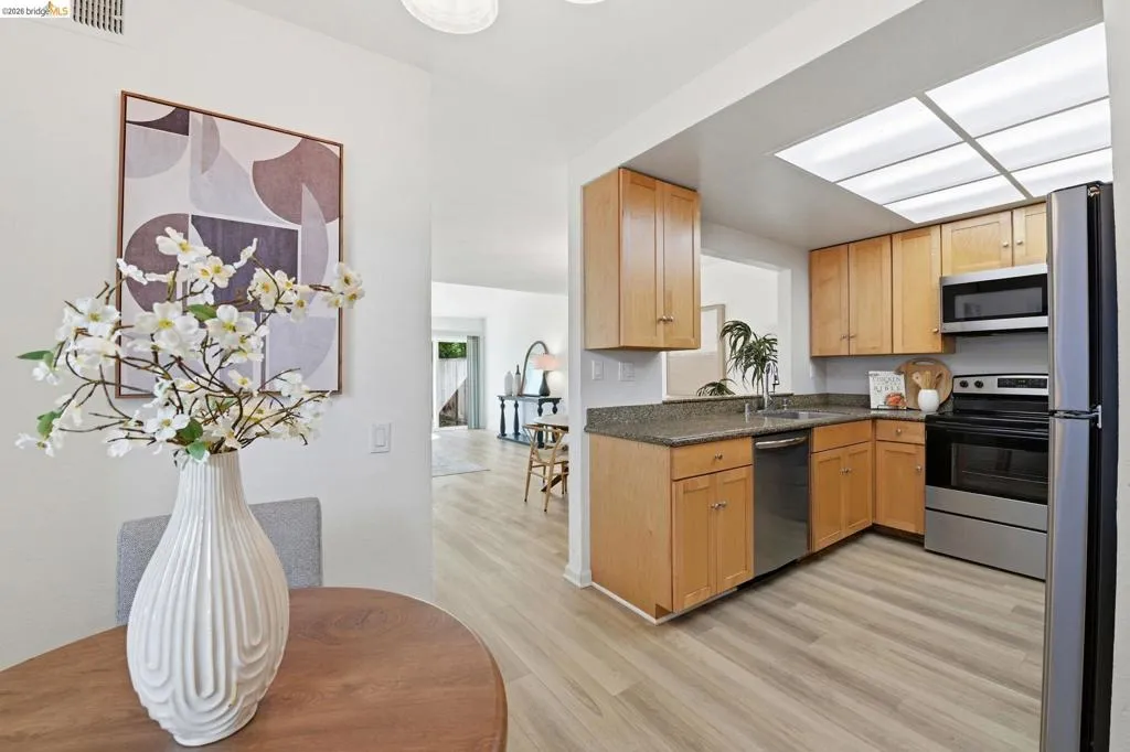 Kitchen area featuring light wood-finish cabinetry, stainless steel appliances, granite-style countertops, and wood-finish flooring