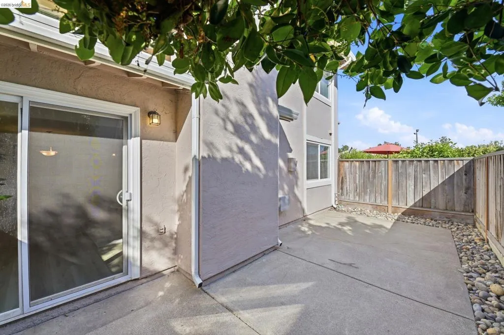 Private concrete patio featuring a wood fence, decorative river rock landscaping, and exterior wall sconce lighting
