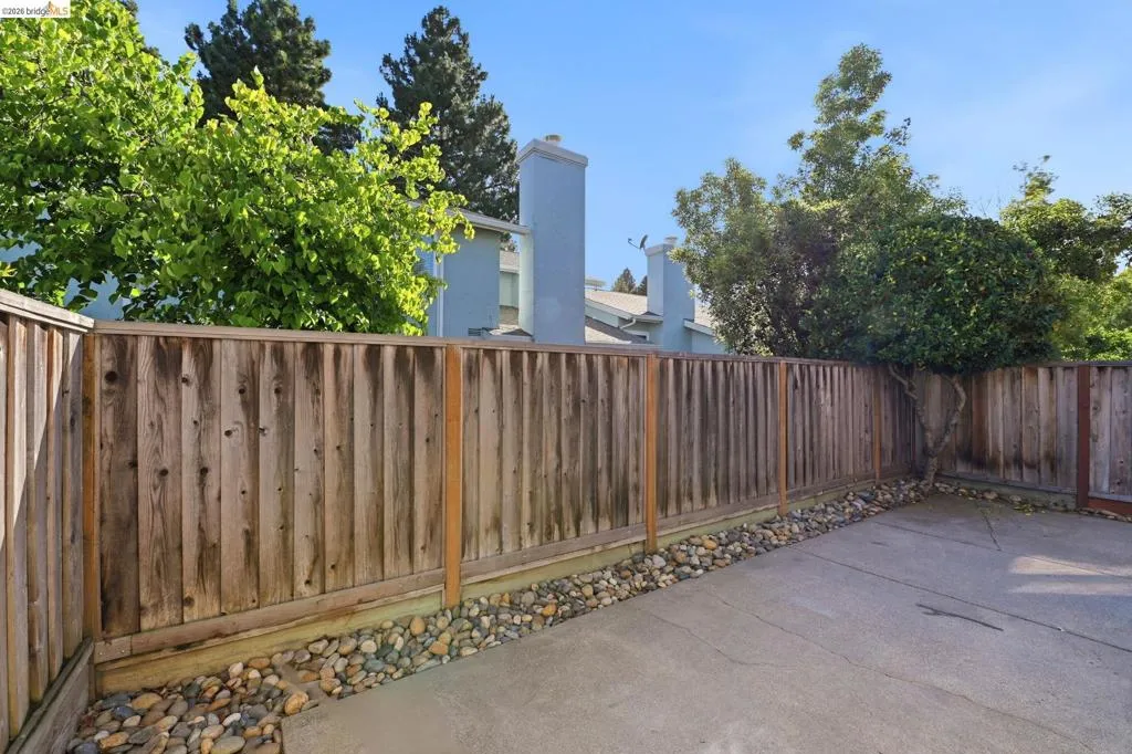 Private concrete patio area with a wooden fence boundary, accented by river rock landscaping and mature greenery