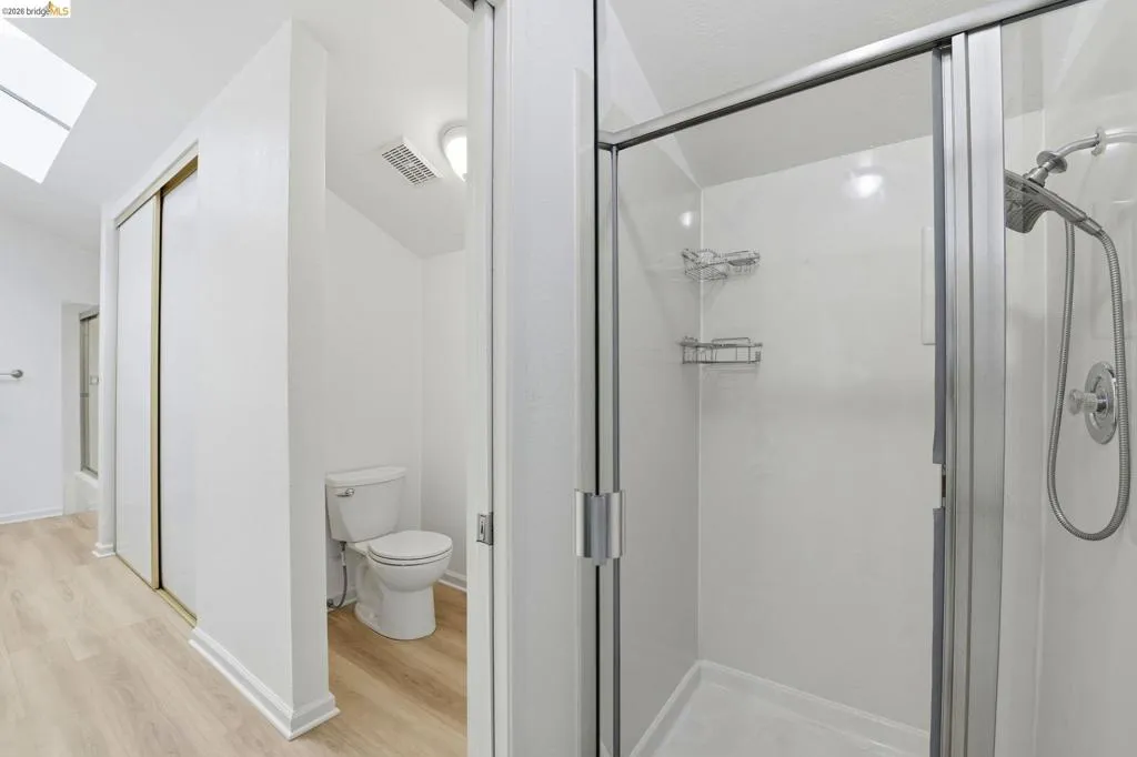 Glass-enclosed shower with chrome fixtures and integrated shelving, featuring a separate toilet area