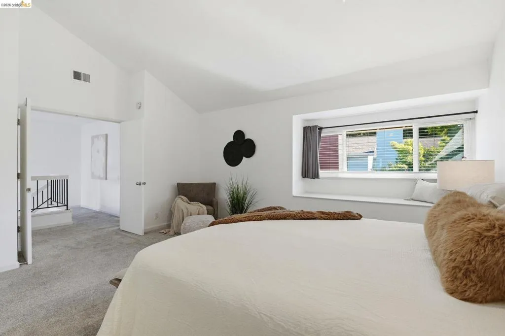 Vaulted ceiling room featuring light-toned carpet, a built-in window bench, and two white doors