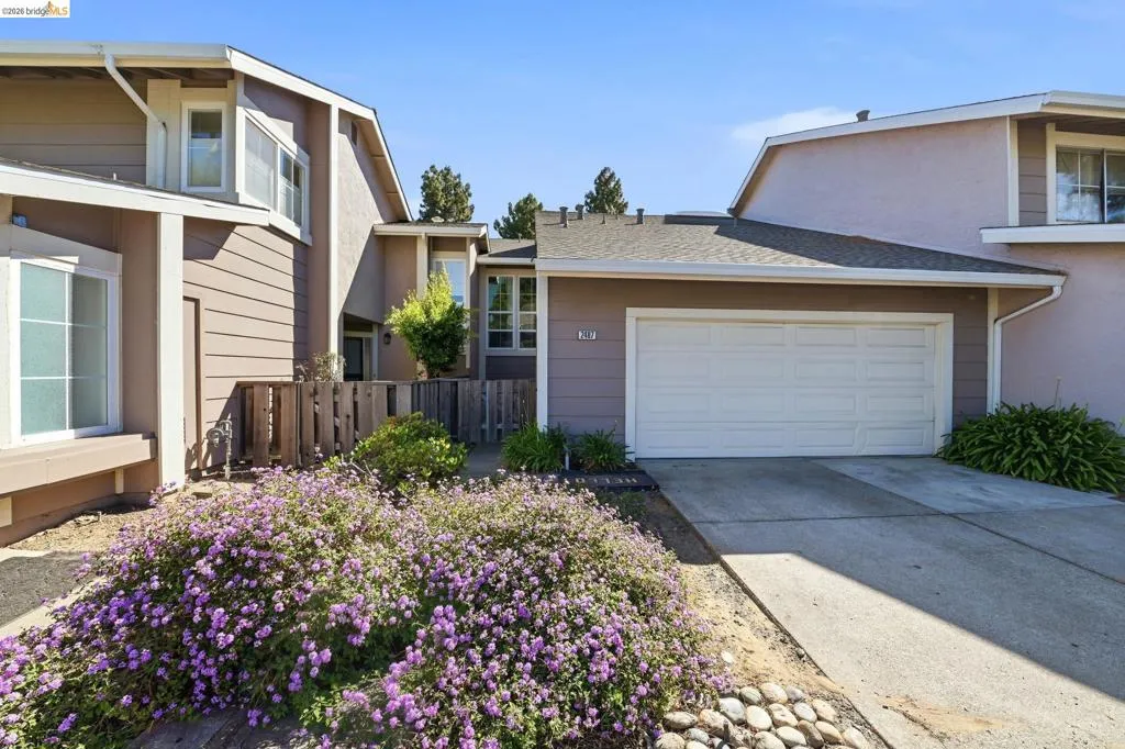 Exterior facade featuring a two-car garage, concrete driveway, and front landscaping with purple flowering plants