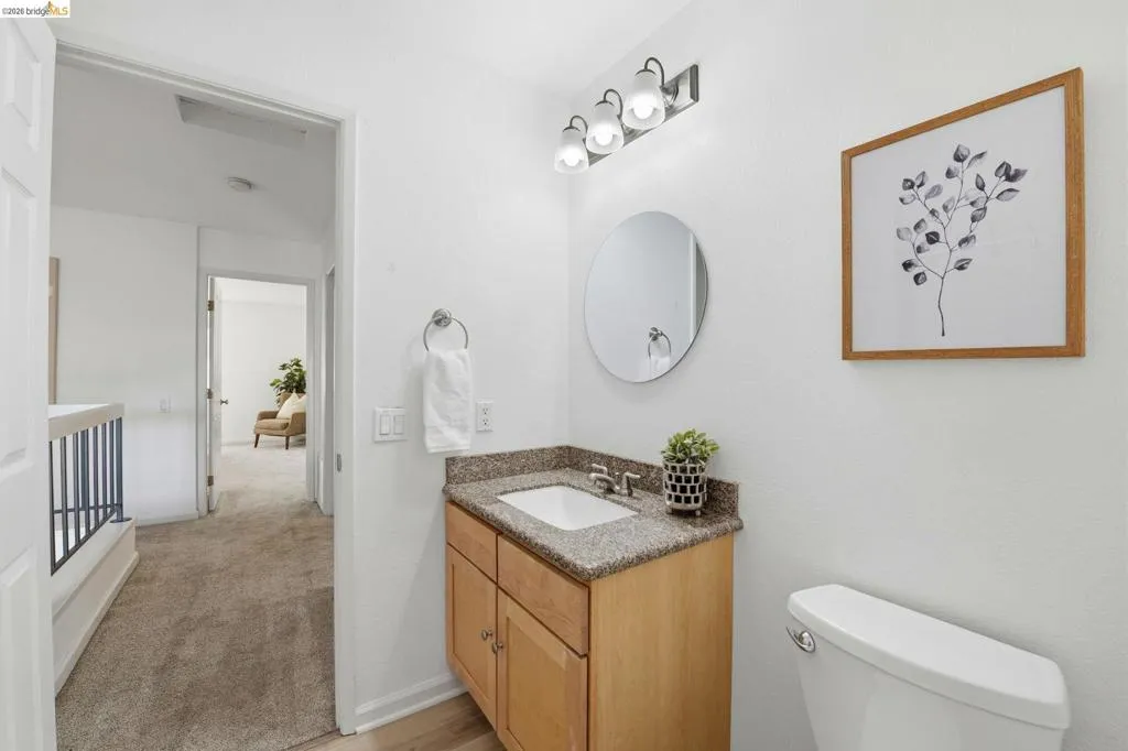 Bathroom featuring a wood-finish vanity with a stone-finish countertop, undermount sink, and a circular mirror
