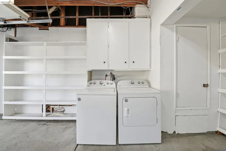 Laundry area with overhead white cabinetry, built-in shelving, and a concrete floor