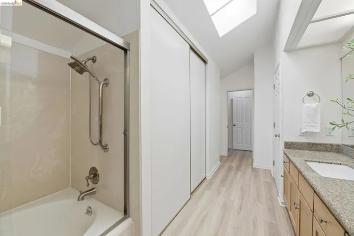 Bathroom featuring a tub and shower combination with a glass enclosure, a vanity with a stone countertop, a rectangular sink, and wood-finish flooring