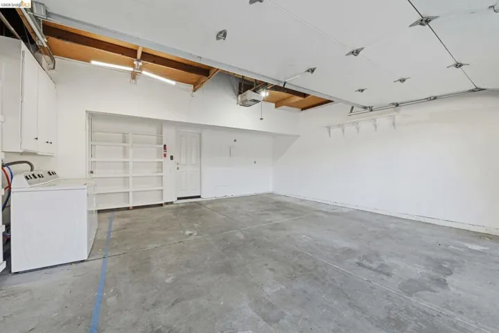 Spacious garage featuring a concrete floor, built-in shelving, white cabinetry, overhead lighting, and an access door