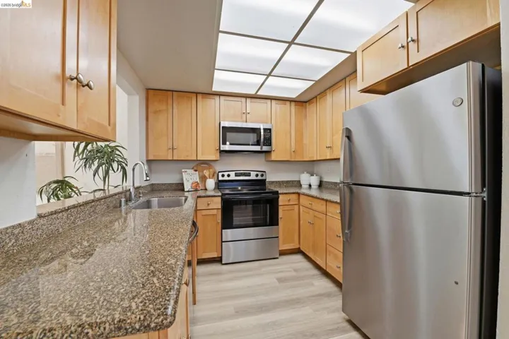 Kitchen featuring light wood cabinetry, granite-style countertops, stainless steel appliances, and wood-finish flooring