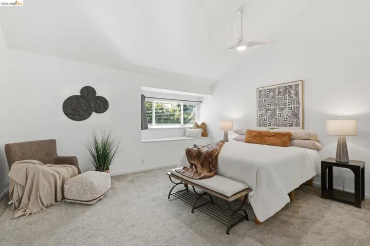 Vaulted ceiling bedroom featuring a built-in window bench, modern ceiling fan, and light gray carpeting