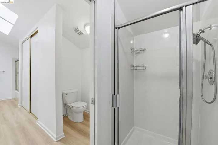 Glass-enclosed shower with chrome fixtures and integrated shelving, featuring a separate toilet area