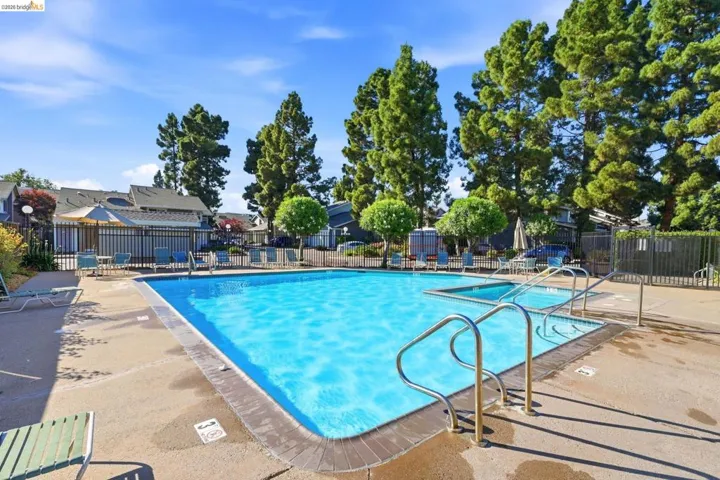 Community swimming pool with an integrated spa, surrounded by a concrete deck and mature trees