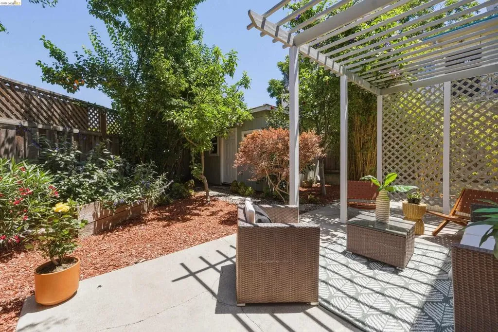 Outdoor patio area featuring a white slatted pergola, concrete paving, and a decorative trellis