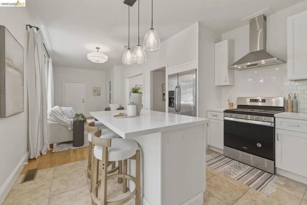 Modern kitchen featuring a white island with a light-toned countertop, pendant lighting, stainless steel appliances, and white shaker-style cabinetry