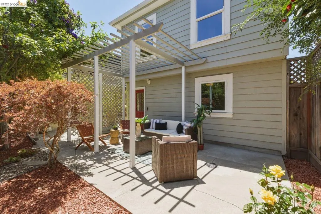 Concrete patio featuring a white pergola structure, lattice privacy screen, and a red entry door