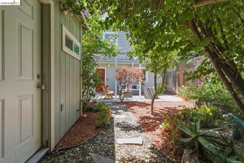 Landscaped outdoor area featuring a stone pathway, mature trees, and garden beds
