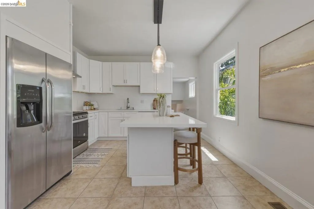 Kitchen featuring stainless steel appliances, white cabinetry, a central island with a solid surface countertop, tile flooring, and a pendant light fixture