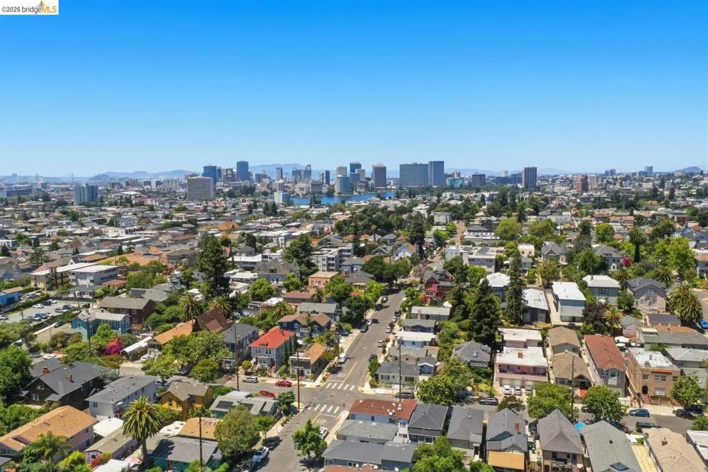 Expansive urban landscape featuring a mix of residential properties with mature trees, established streets, and a distant cityscape with a prominent body of water