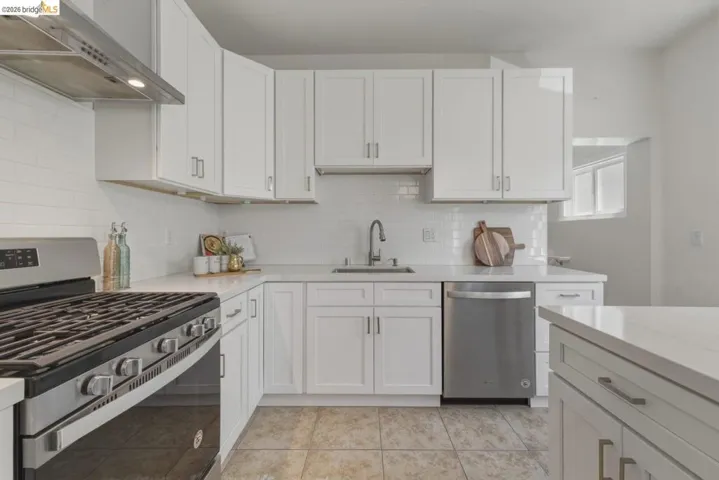 Modern kitchen featuring white shaker cabinetry, stainless steel appliances, a subway tile backsplash, light-toned countertops, and tile flooring