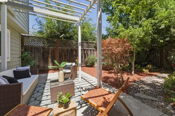 Outdoor patio featuring a white pergola structure, concrete paving, and a decorative area rug