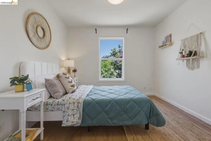 Bright bedroom featuring a white upholstered headboard, wood-finish flooring, a single window with white trim, and light-colored walls