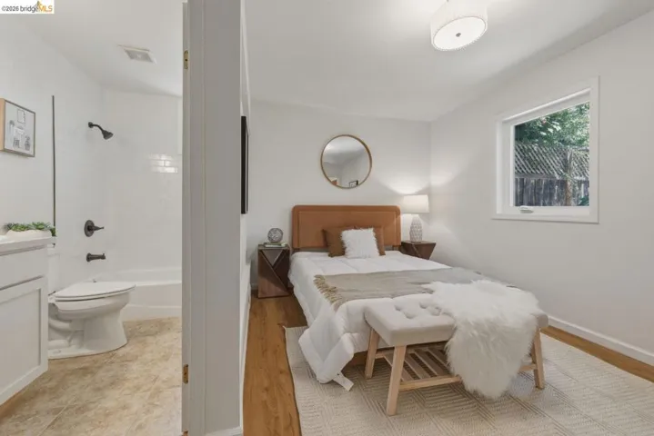 Bedroom featuring wood-finish flooring and a white window with exterior fence visibility