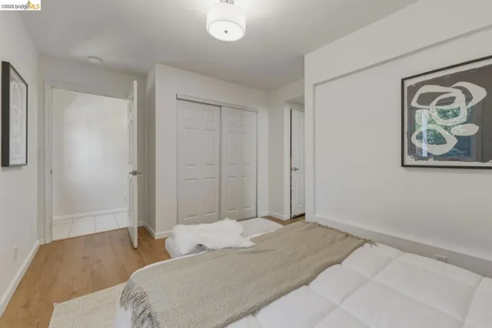 Bright bedroom featuring light wood-finish flooring, white walls, a modern ceiling light fixture, and bifold closet doors
