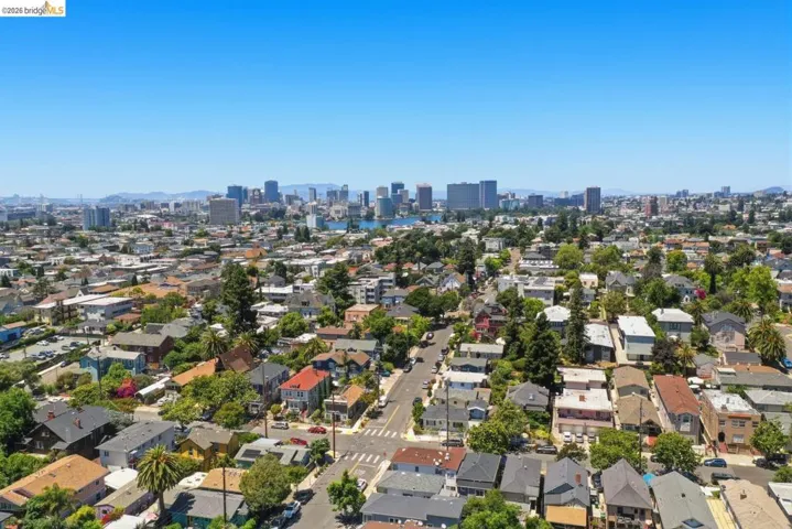 Expansive urban landscape featuring a mix of residential properties with mature trees, established streets, and a distant cityscape with a prominent body of water