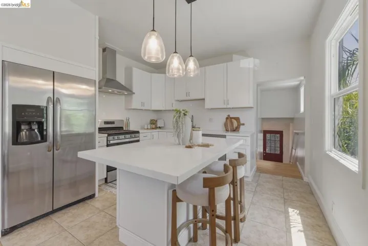 Modern kitchen featuring a white center island with a solid surface countertop, white cabinetry, stainless steel appliances, and pendant lighting