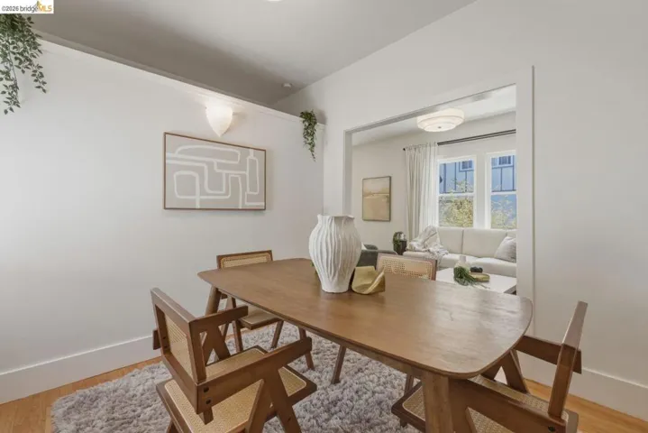 Dining area featuring hardwood flooring, white baseboards, and a pass-through opening to an additional room with a double window