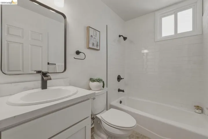 Bathroom featuring a white subway tile surround, white vanity with an undermount sink, matte black fixtures, and a window above the tub