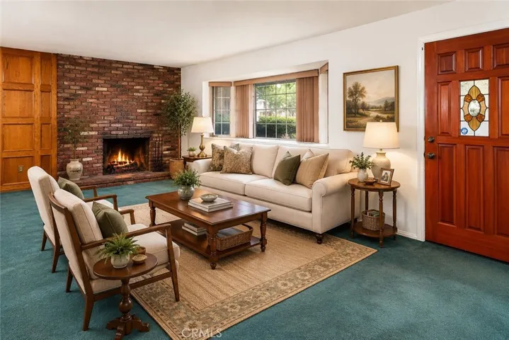 Natural light pours through the large picture window in the living room, while the floor-to-ceiling brick fireplace creates a comfortable focal point for the space. Photo is virtually staged.