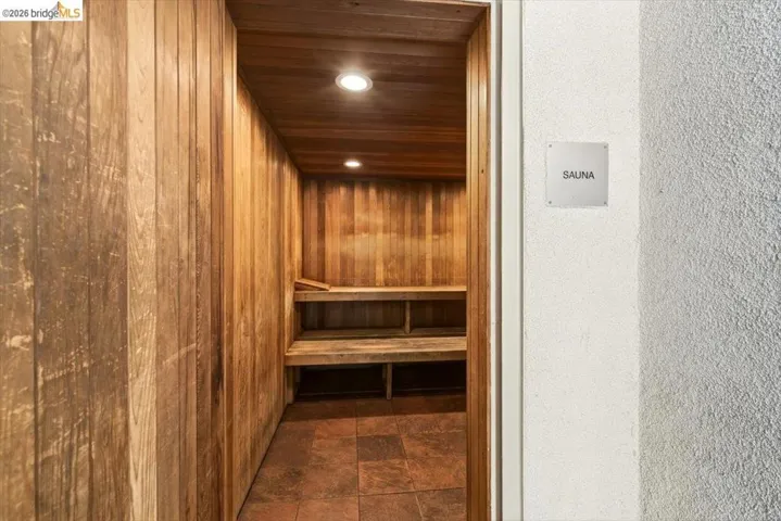 Dedicated sauna room featuring natural wood paneling, built-in wooden benches, recessed ceiling lighting, and tiled flooring
