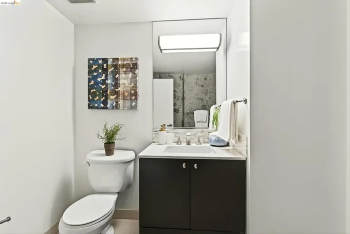Contemporary bathroom featuring a white toilet, dark wood-finish vanity with a white countertop and integrated sink, and a large mirror with a rectangular overhead light fixture