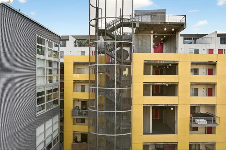 Modern multi-story building exterior featuring a yellow facade, red entry doors, and a prominent exterior spiral staircase