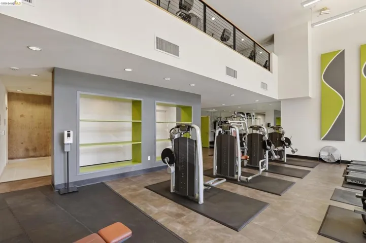 Fitness center featuring contemporary lime green and grey accent walls, recessed lighting, a mezzanine level with additional equipment, and built-in shelving