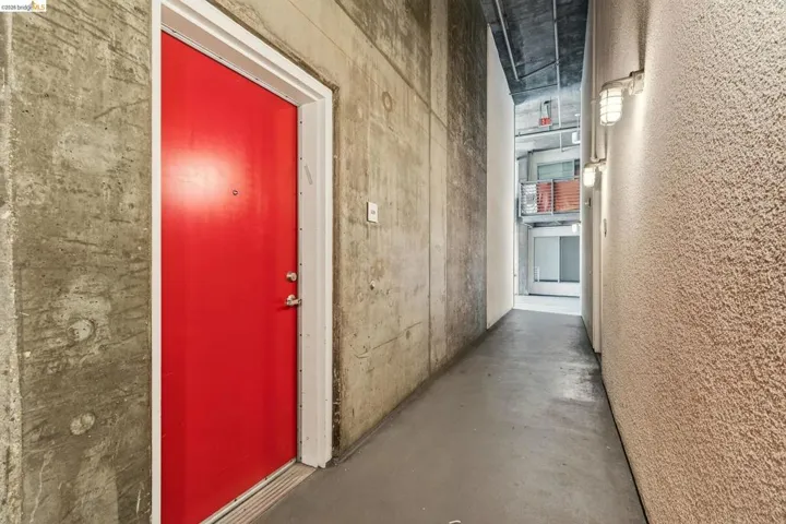 Vibrant red entry door framed by a white trim, set against a raw concrete wall