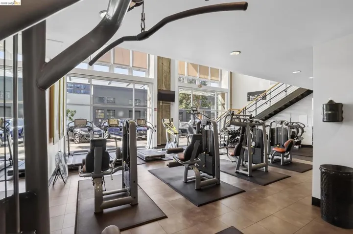Fitness center featuring a variety of exercise equipment, expansive windows, high ceilings, a wall-mounted television, and a modern staircase