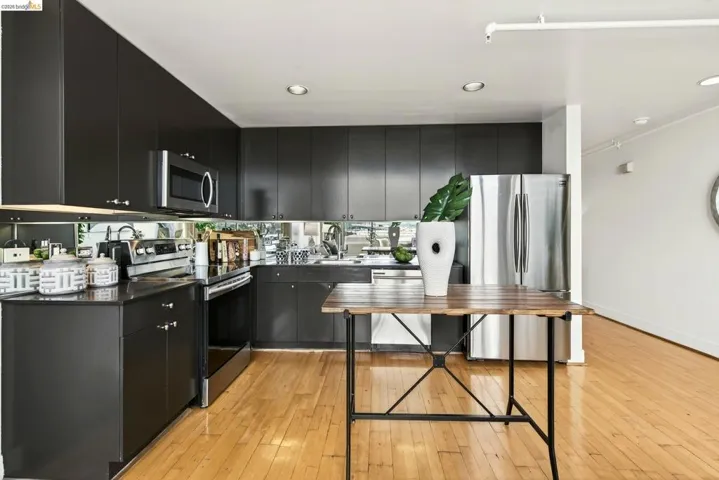 Modern kitchen featuring dark cabinetry with brushed nickel hardware, stainless steel appliances, a mirrored backsplash, and wood-finish flooring