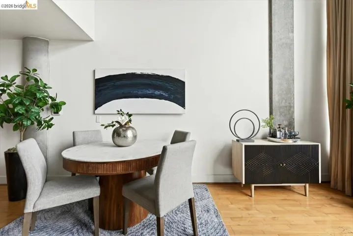 Dining area featuring a wood-finish oval table with a light-colored surface, light grey upholstered chairs, and wood-finish flooring