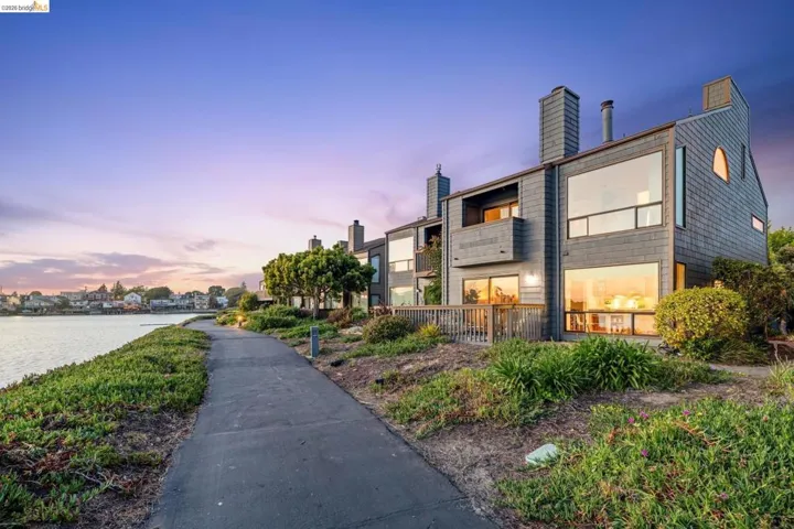 Contemporary waterfront residence featuring a shingle exterior, expansive windows, a private deck, and a path along the water