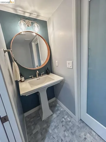 Pedestal sink with polished chrome faucet and a circular mirror featuring a wood-finish frame